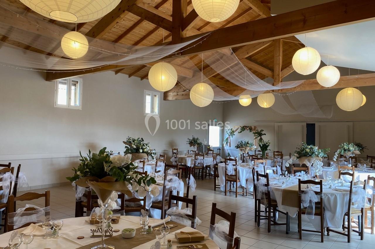 Salle de réception décorée avec des tables dressées, des chaises ornées de voilages blancs et des lanternes suspendues.