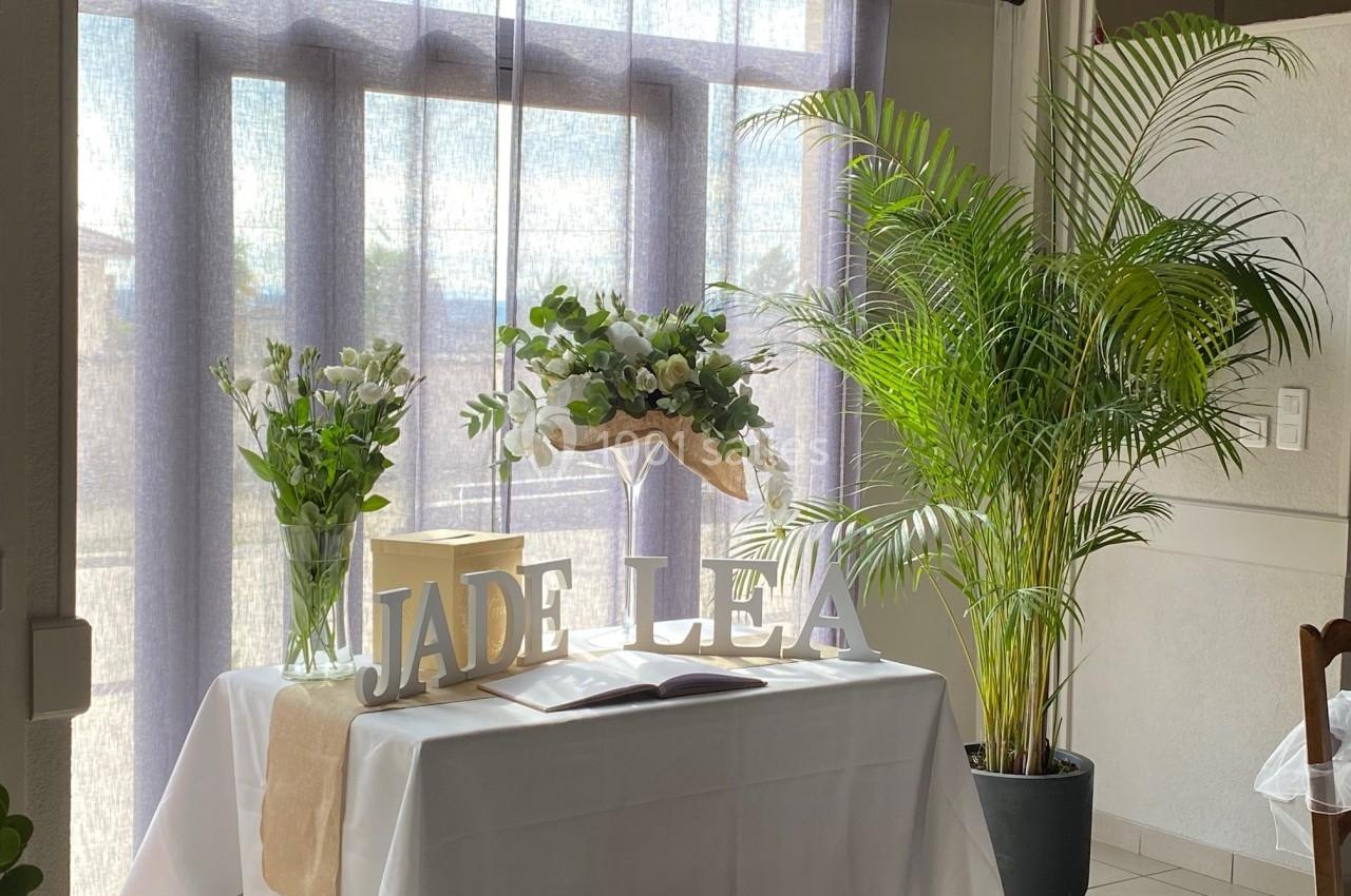Table décorée avec des fleurs, des plantes en pot et les lettres ’JADE LEA’ devant une fenêtre avec rideaux translucides.