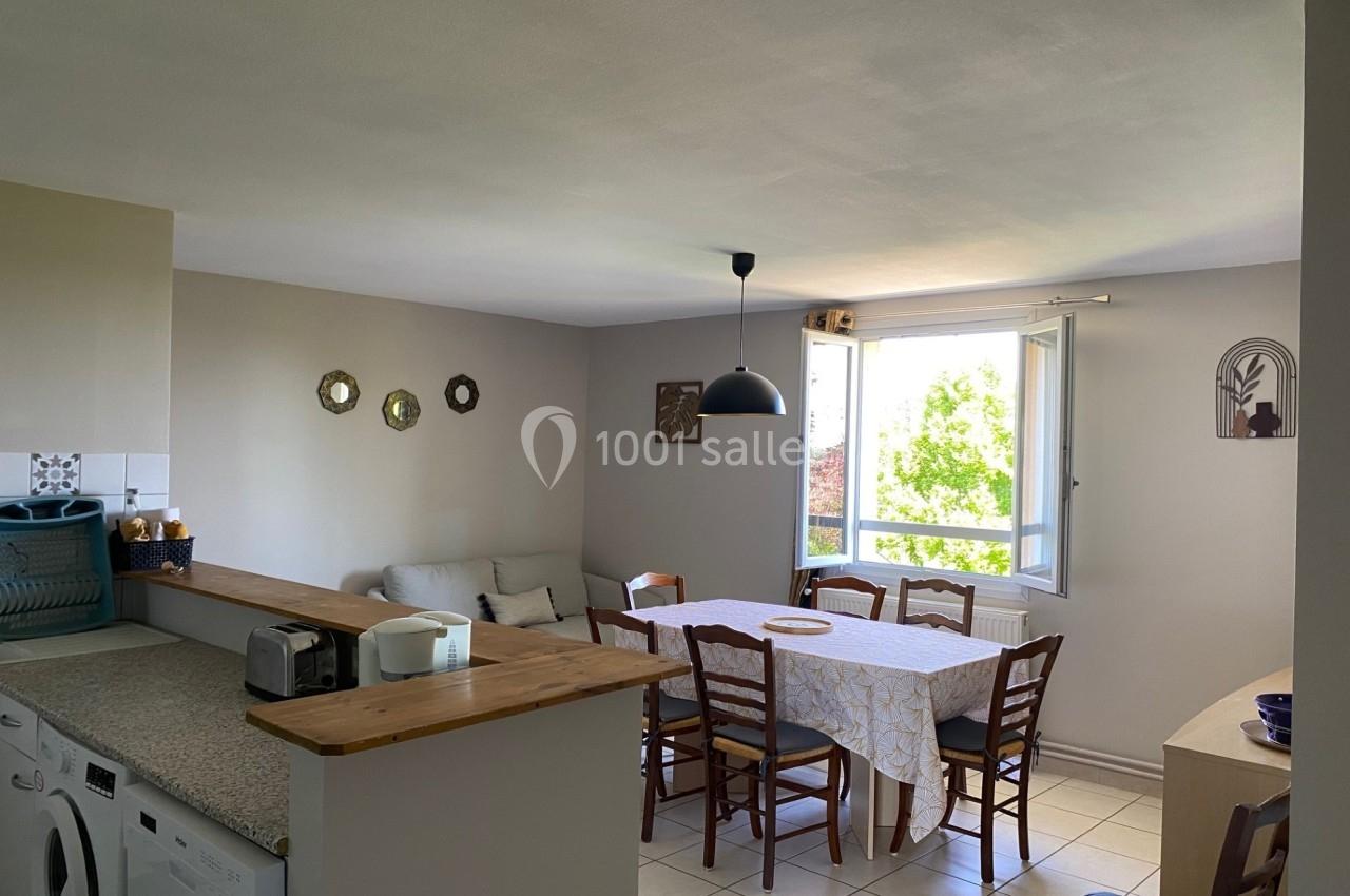 Salle à manger lumineuse avec table, chaises en bois, canapé, fenêtre ouverte et décoration murale sobre.