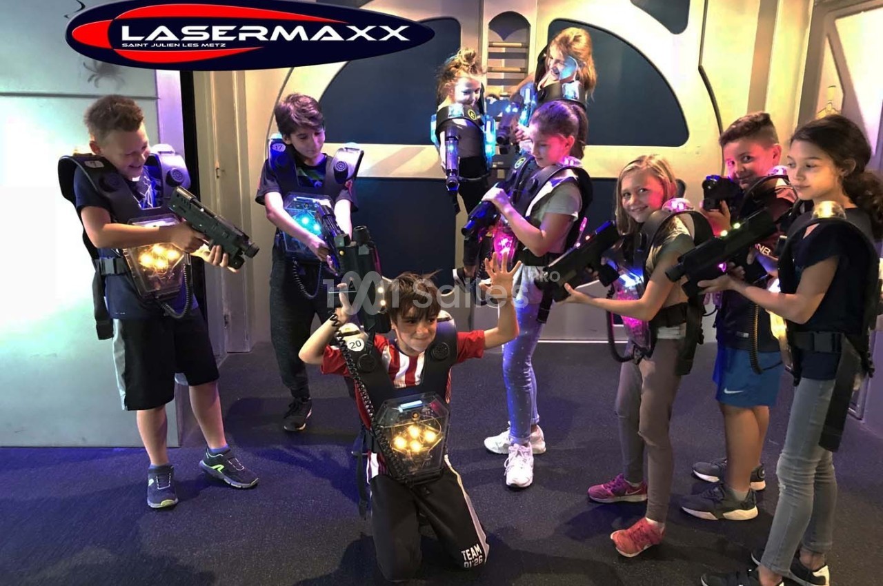 Des enfants équipés de gilets et pistolets lumineux jouent au laser game dans une salle aux décors futuristes.