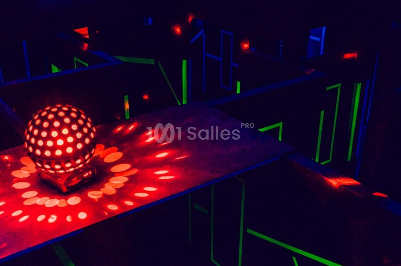 Salle sombre de laser game avec des lumières rouges et vertes, et une sphère lumineuse au centre.