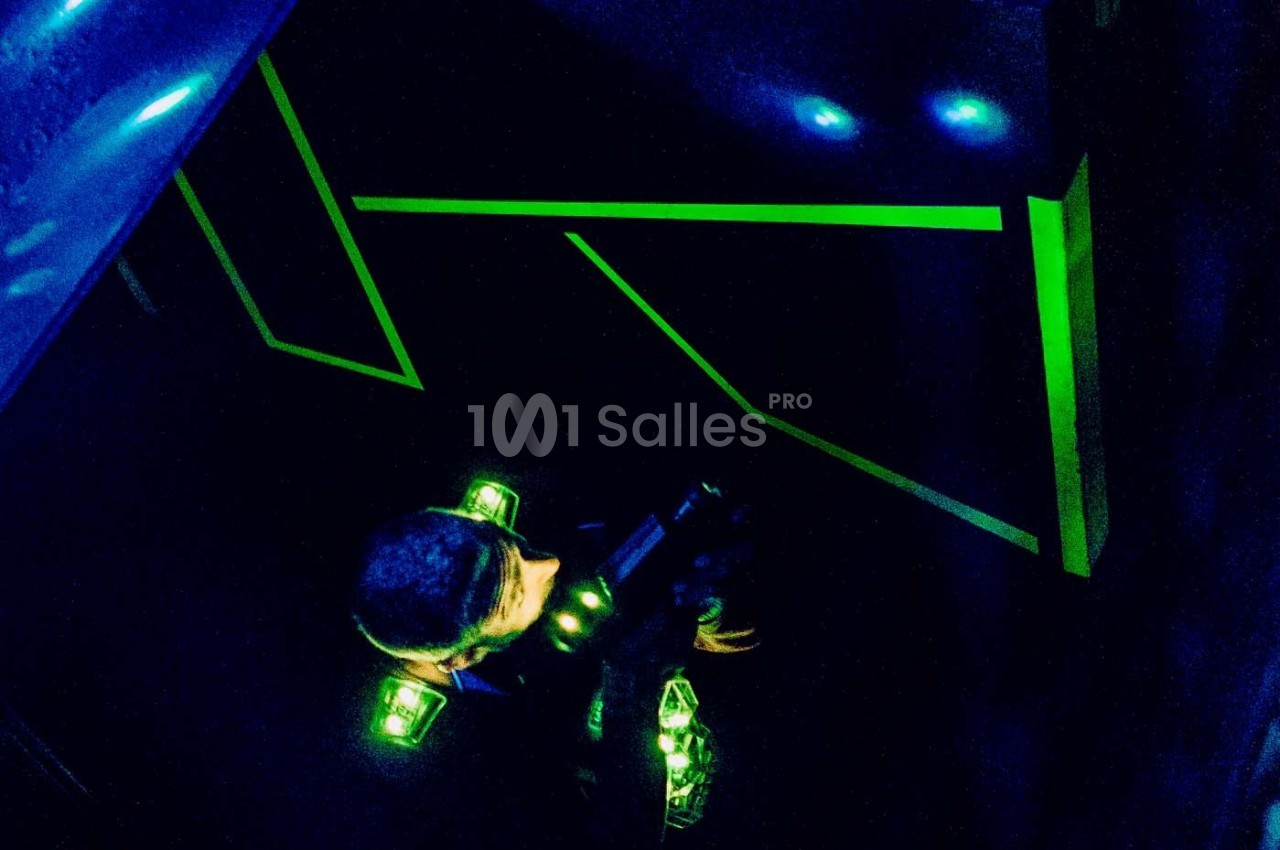 Personne jouant au laser game dans une salle sombre avec des lumières fluorescentes vertes.