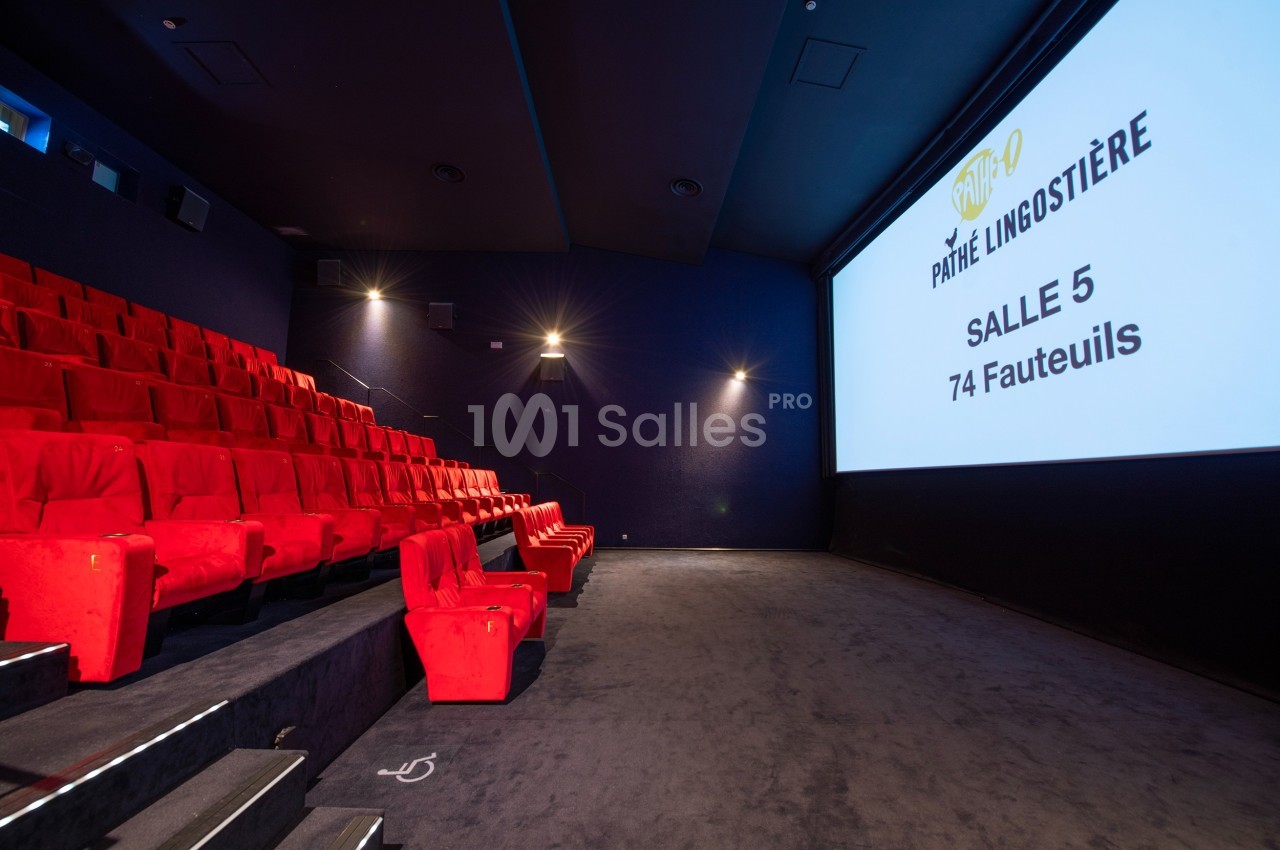 Salle de cinéma avec des sièges rouges, écran blanc affichant ’Salle 5, 74 fauteuils’ et éclairage tamisé.
