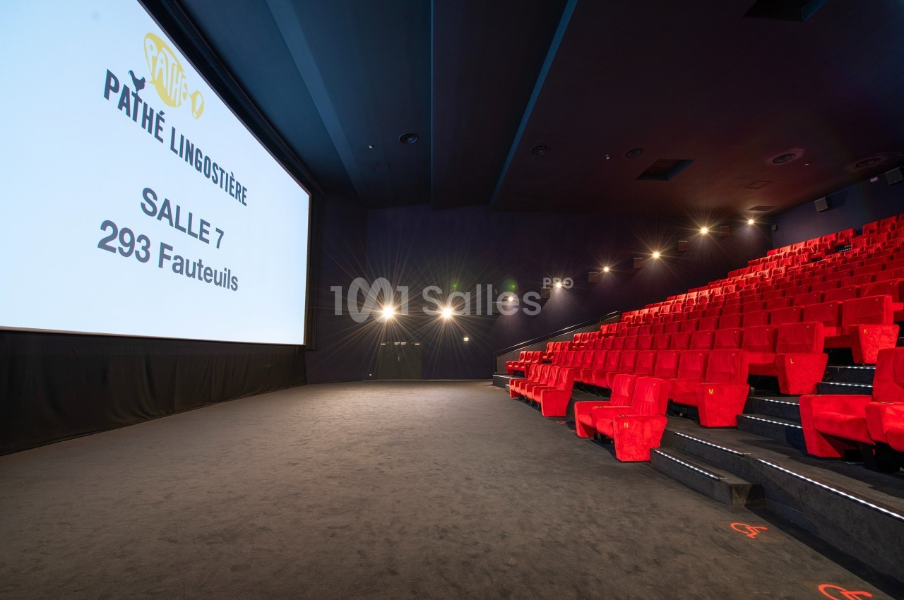 Salle de cinéma moderne avec écran géant, rangées de fauteuils rouges et éclairage tamisé.