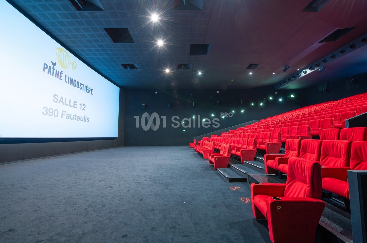 Salle de cinéma moderne avec écran géant, rangées de fauteuils rouges et éclairage tamisé.