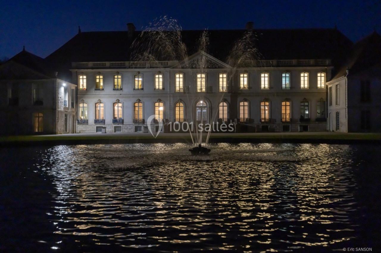 Façade éclairée d'un bâtiment historique avec une fontaine illuminée au premier plan, de nuit.