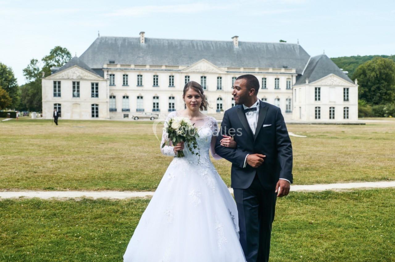 Un couple en tenue de mariage marche dans un parc devant un grand bâtiment historique.