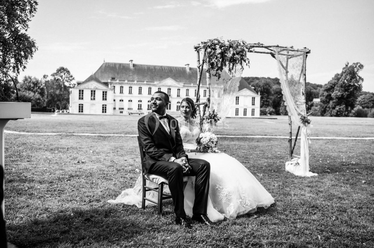 Un couple assis sous une arche décorée, dans un jardin devant un grand bâtiment historique.