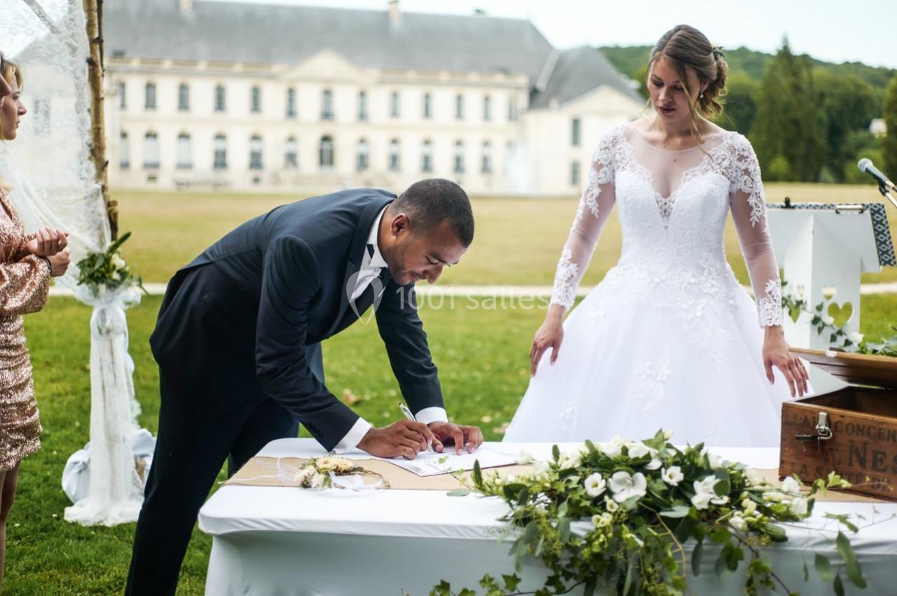 Un couple lors d'une cérémonie de mariage, le marié signe un document sur une table décorée de fleurs.