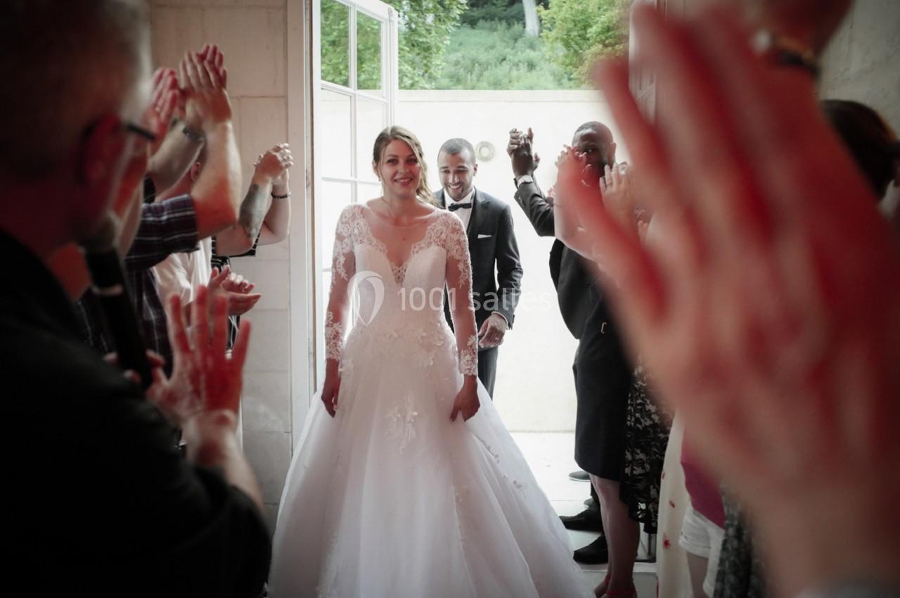 Un couple de mariés souriant sort d'un bâtiment sous les applaudissements des invités.
