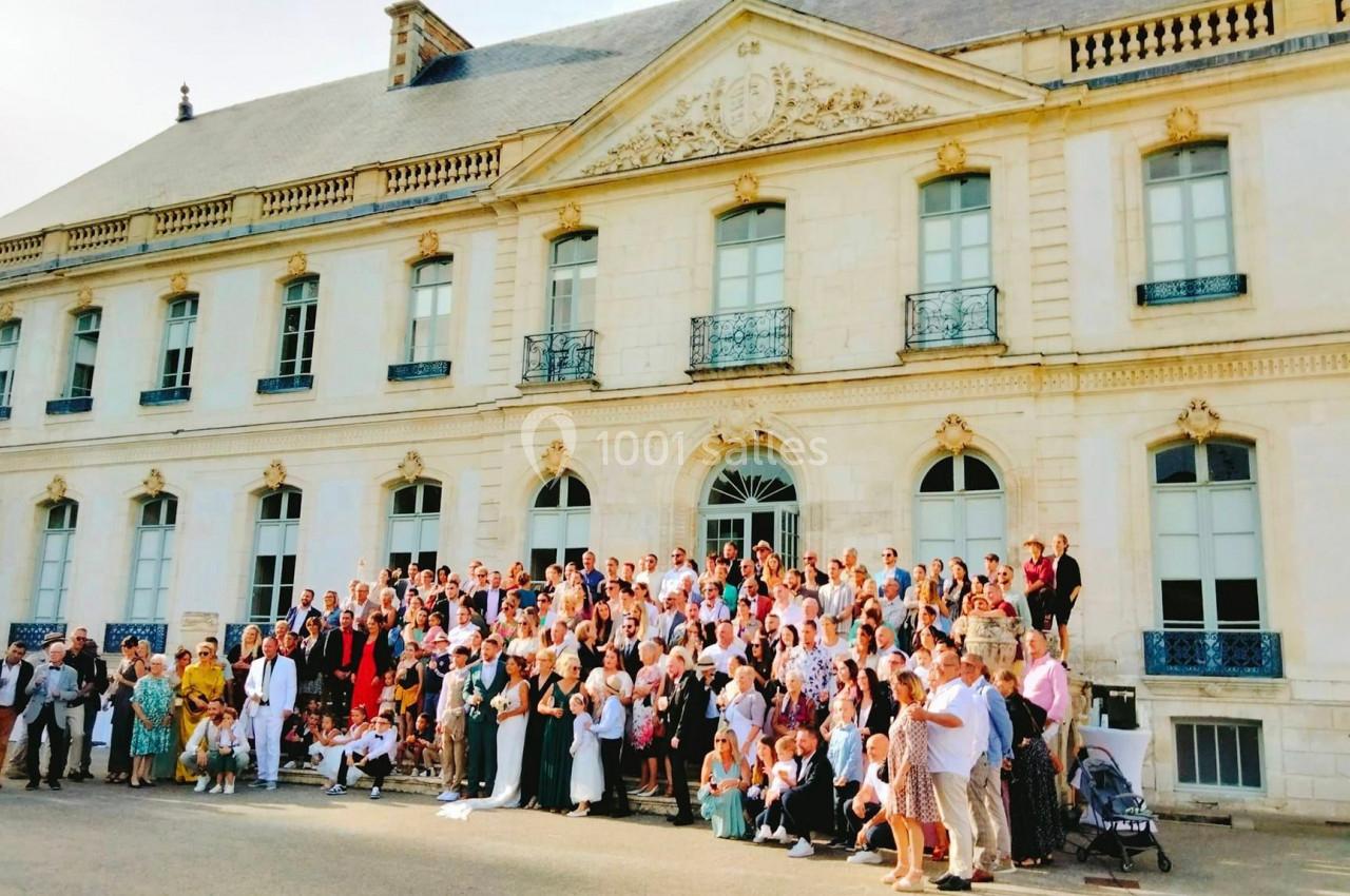 Un grand groupe de personnes posant devant un bâtiment historique en pierre avec des fenêtres et des balcons.