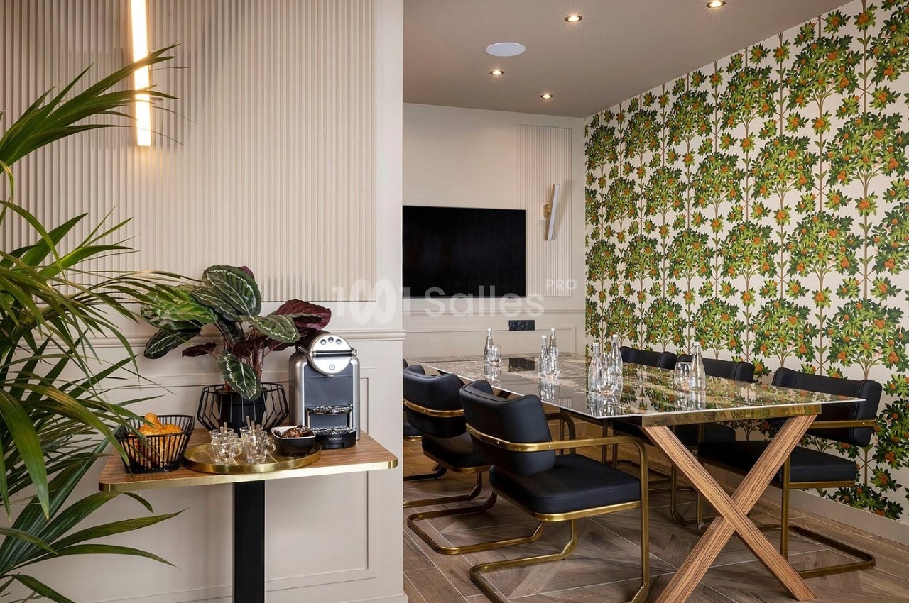 Salle à manger moderne avec table en verre, chaises noires, mur à motif floral et coin café avec machine à expresso.