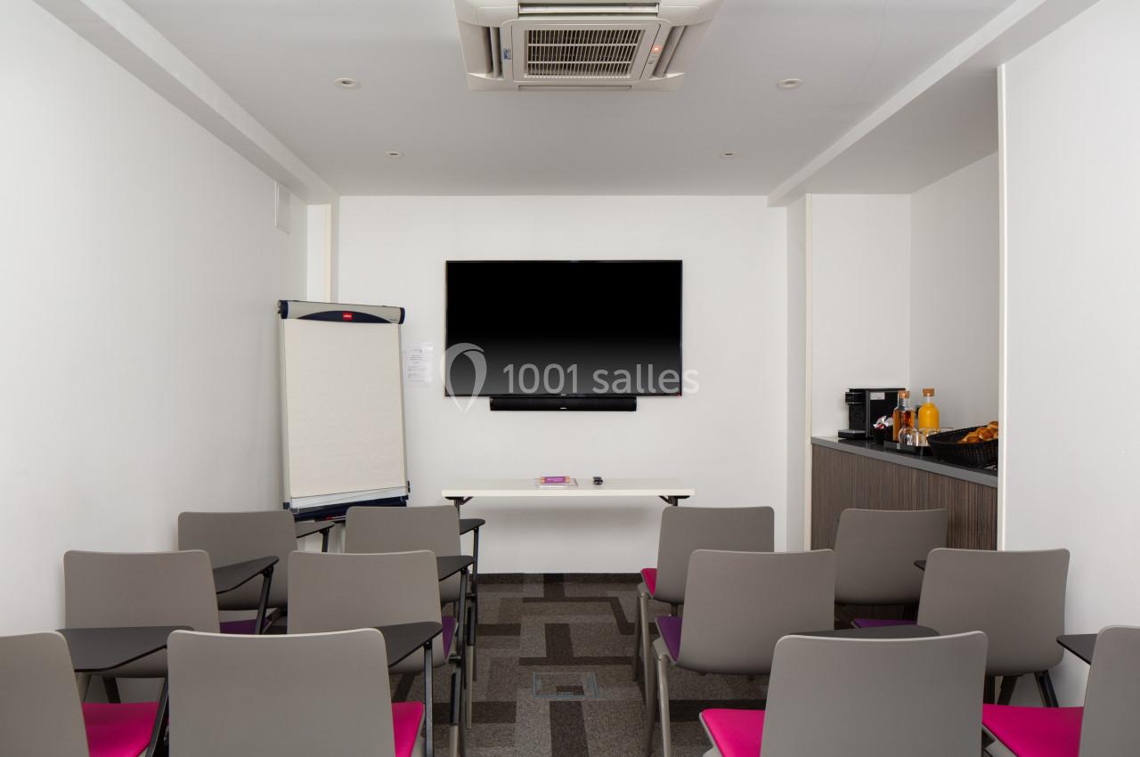 Salle de réunion équipée de chaises, écran mural, paperboard et coin rafraîchissements avec boissons et collations.