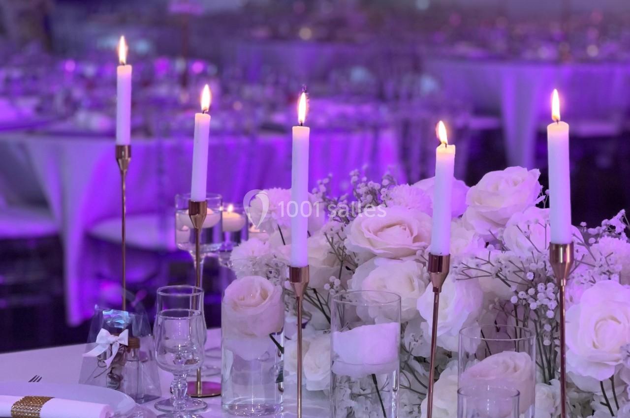Location salle Beauchamp (Val-d'Oise) - Les Salons Beauchamp #25 Table élégamment dressée avec chandeliers, roses blanches et vaisselle raffinée dans une salle décorée pour un événement.