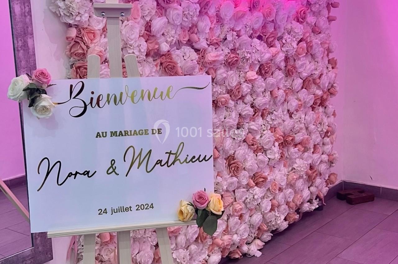 Location salle Beauchamp (Val-d'Oise) - Les Salons Beauchamp #18 Mur de fleurs roses avec un panneau sur chevalet annonçant un mariage, éclairage néon en arrière-plan.