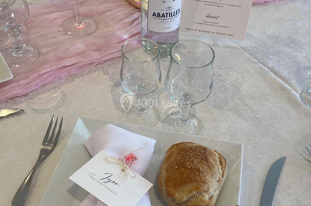 Location salle Beauchamp (Val-d'Oise) - Les Salons Beauchamp #22 Table dressée avec une assiette carrée, serviette pliée, pain, menu, bougie, et bouteille d'eau minérale.