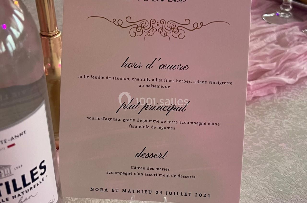 Location salle Beauchamp (Val-d'Oise) - Les Salons Beauchamp #21 Carte de menu de mariage posée sur une table décorée avec des bougies, nappes blanches et éléments roses.