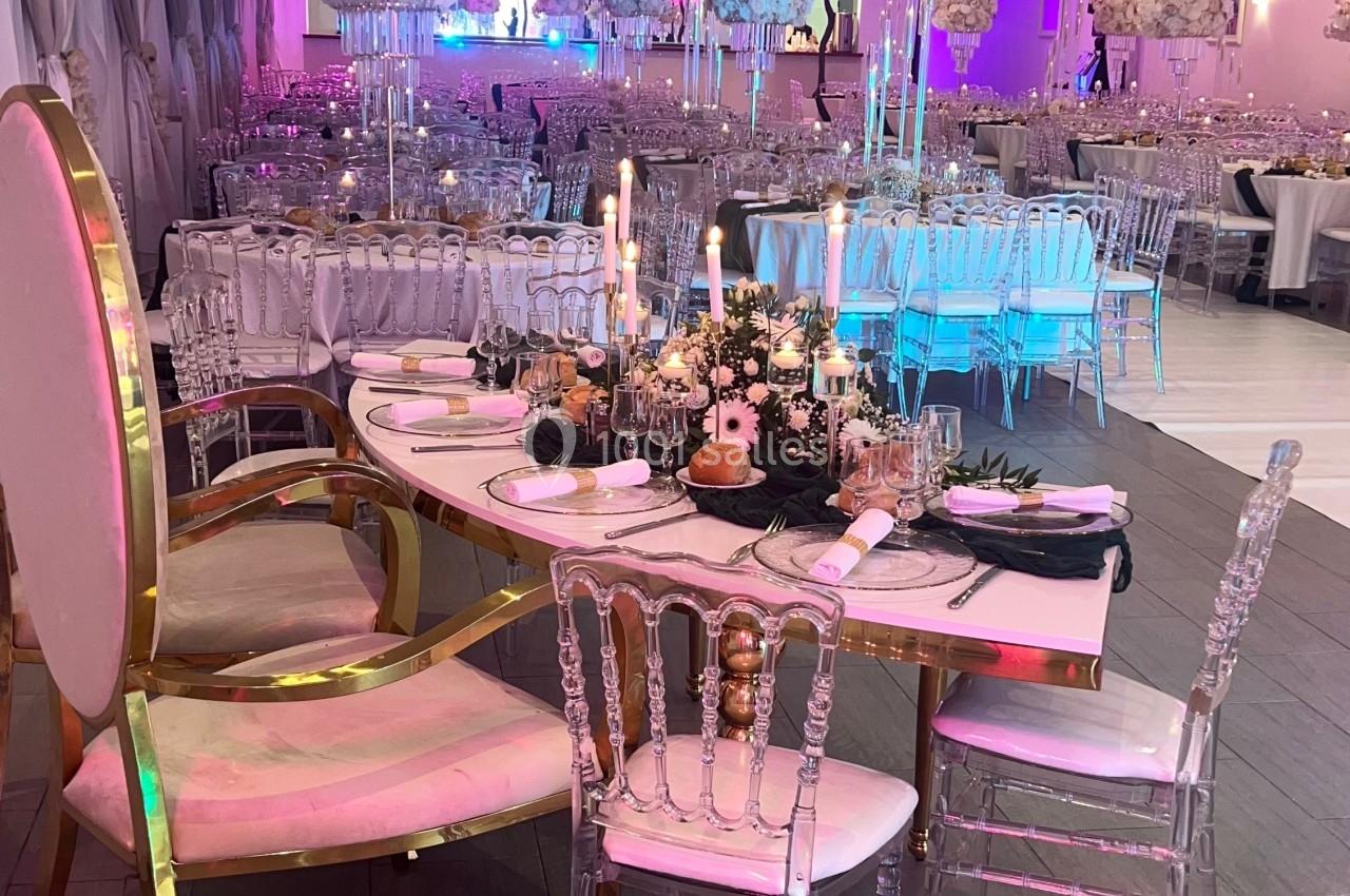 Location salle Beauchamp (Val-d'Oise) - Les Salons Beauchamp #40 Salle de réception décorée avec des tables élégantes, des chandeliers et des chaises transparentes sous un éclairage coloré.