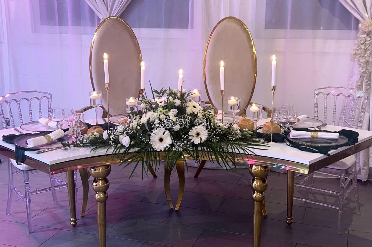 Location salle Beauchamp (Val-d'Oise) - Les Salons Beauchamp #23 Table élégante décorée de fleurs blanches, bougies allumées et chaises transparentes, devant des rideaux clairs.