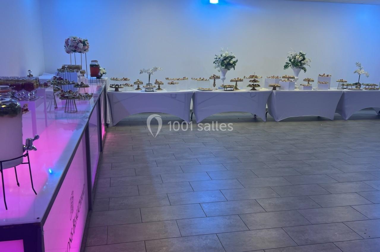 Location salle Beauchamp (Val-d'Oise) - Les Salons Beauchamp #33 Buffet de desserts variés disposés sur des tables blanches dans une salle éclairée par des lumières colorées.
