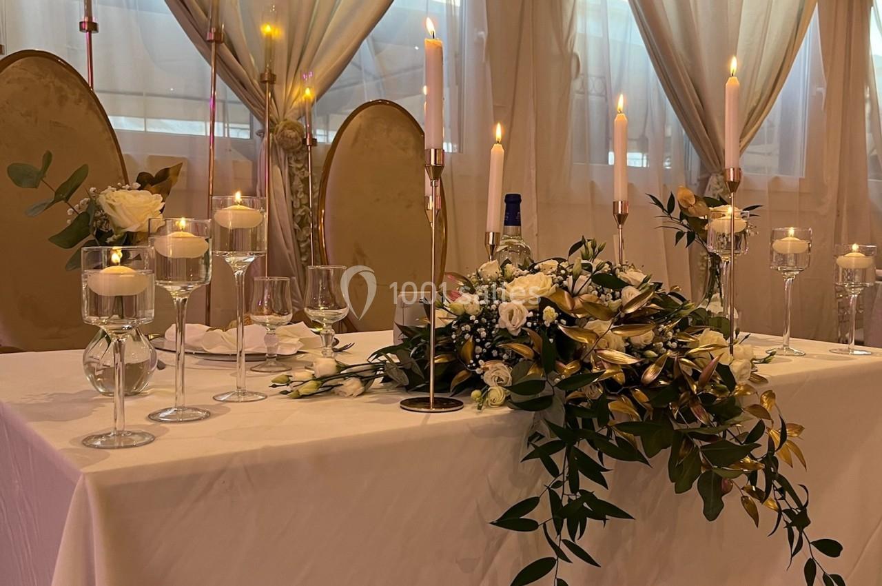 Location salle Beauchamp (Val-d'Oise) - Les Salons Beauchamp #28 Table décorée pour un mariage avec nappes blanches, bougies allumées, fleurs et chaises dorées en arrière-plan.