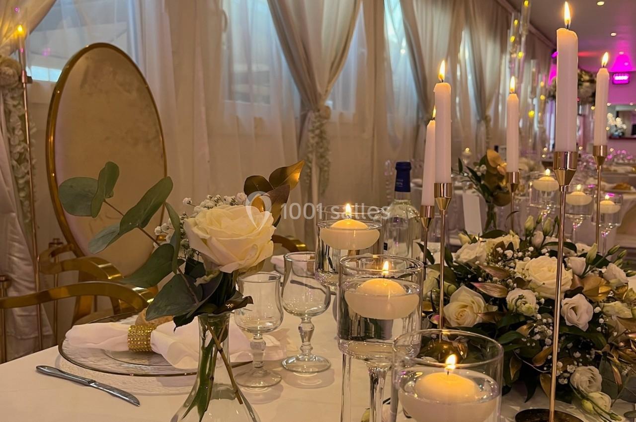 Location salle Beauchamp (Val-d'Oise) - Les Salons Beauchamp #32 Table élégamment décorée avec des bougies allumées, des fleurs blanches et des verres, dans une salle aux rideaux clairs.