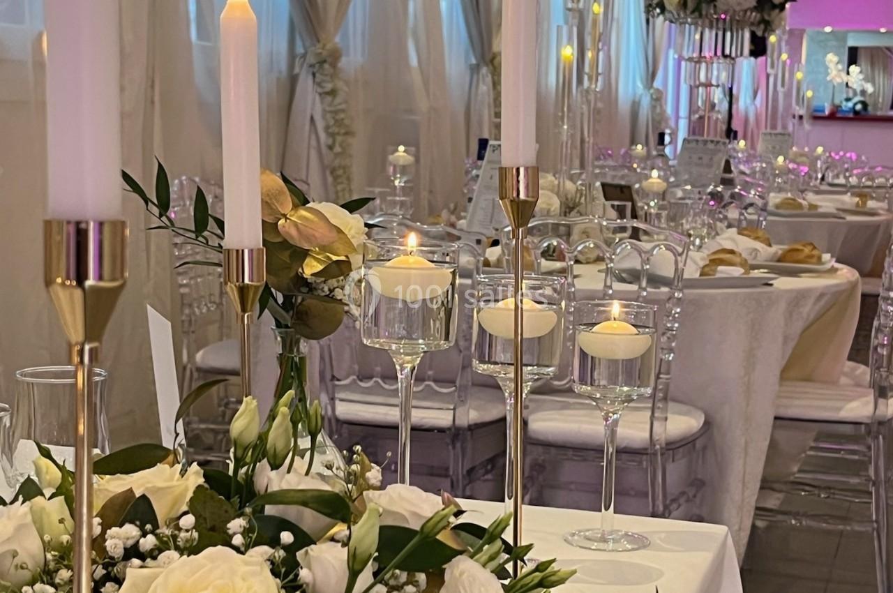 Location salle Beauchamp (Val-d'Oise) - Les Salons Beauchamp #30 Salle de réception élégante avec tables décorées de fleurs blanches, bougies allumées et chaises transparentes.