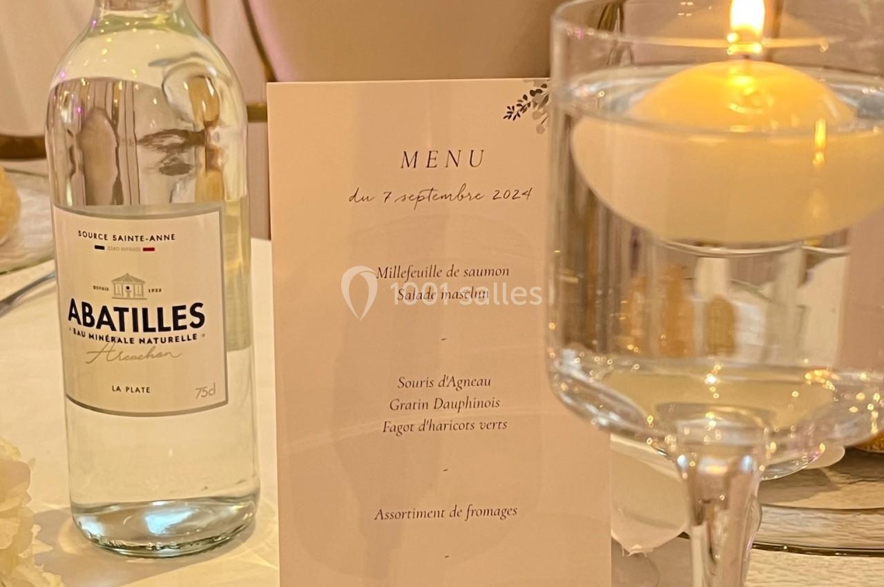 Location salle Beauchamp (Val-d'Oise) - Les Salons Beauchamp #43 Bouteille d'eau, menu imprimé et bougie sur une table élégamment dressée pour un repas.