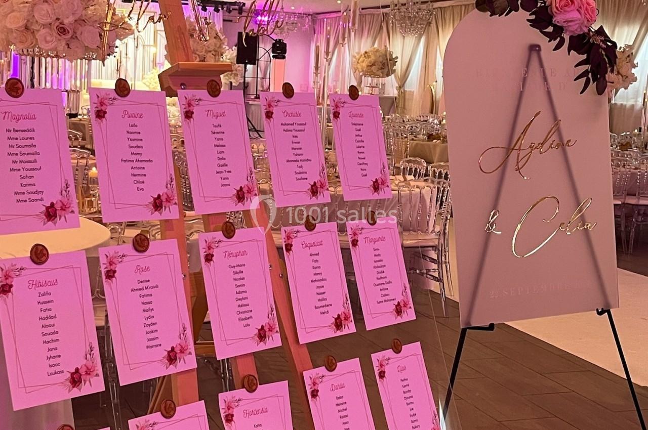 Location salle Beauchamp (Val-d'Oise) - Les Salons Beauchamp #37 Plan de table de mariage avec des listes de noms sur un chevalet en bois et un panneau décoratif à côté, dans une salle…