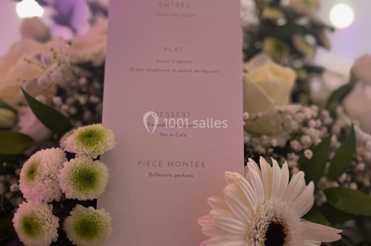 Location salle Beauchamp (Val-d'Oise) - Les Salons Beauchamp #29 Menu imprimé sur une carte blanche entourée de fleurs blanches et vertes dans un décor lumineux.