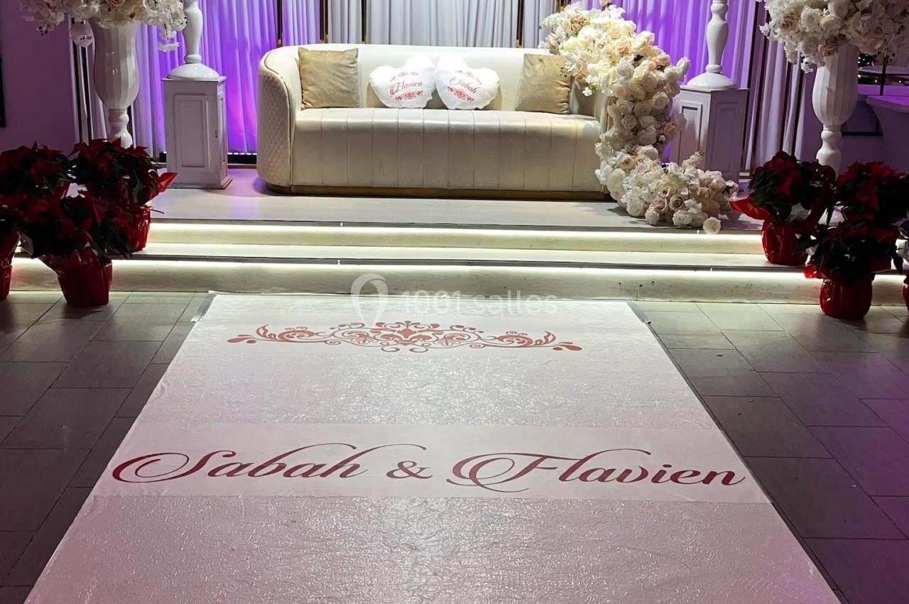 Location salle Beauchamp (Val-d'Oise) - Les Salons Beauchamp #35 Décor de mariage avec canapé beige, fleurs blanches et tapis personnalisé portant des prénoms en rouge.