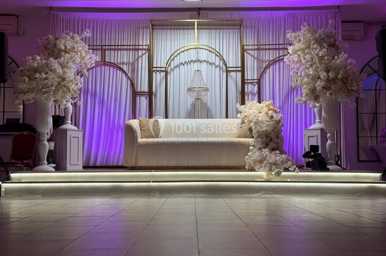 Location salle Beauchamp (Val-d'Oise) - Les Salons Beauchamp #14 Canapé blanc décoré de fleurs blanches, entouré d'arches dorées et éclairé par une lumière violette.