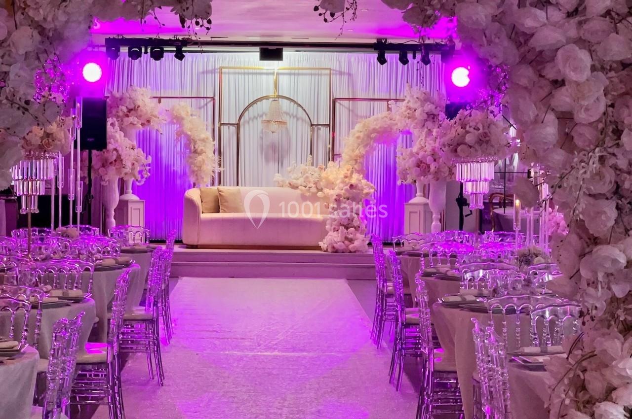 Location salle Beauchamp (Val-d'Oise) - Les Salons Beauchamp #6 Salle de réception décorée avec des arches fleuries, des tables dressées et un éclairage rose.