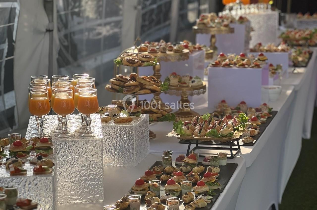 Location salle Beauchamp (Val-d'Oise) - Les Salons Beauchamp #10 Buffet élégant avec verrines, amuse-bouches variés et boissons disposés sur une longue table blanche en extérieur.