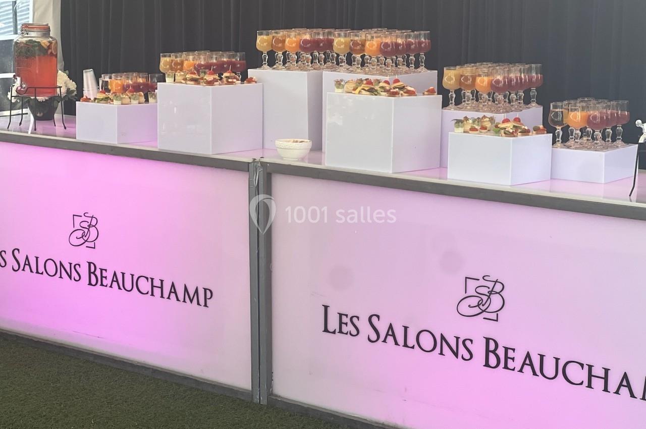 Location salle Beauchamp (Val-d'Oise) - Les Salons Beauchamp #11 Buffet de boissons colorées disposées sur des présentoirs blancs, avec un panneau lumineux ’Les Salons Beauchamp’.