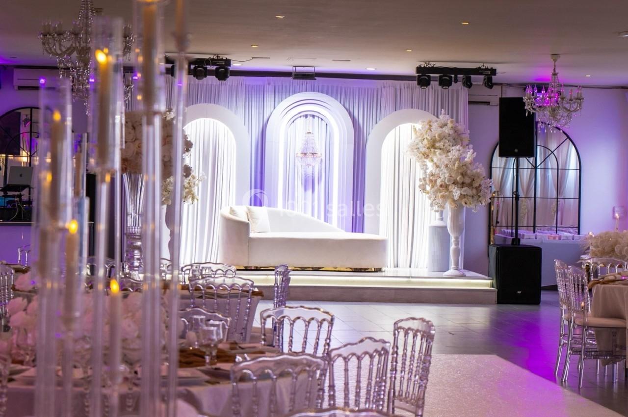 Location salle Beauchamp (Val-d'Oise) - Les Salons Beauchamp #49 Salle de réception élégante avec décoration florale blanche, chandeliers et canapé devant des arches lumineuses.