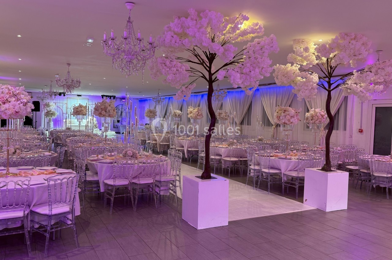 Salle de réception décorée avec des tables élégantes, des chaises transparentes et des arbres artificiels fleuris.