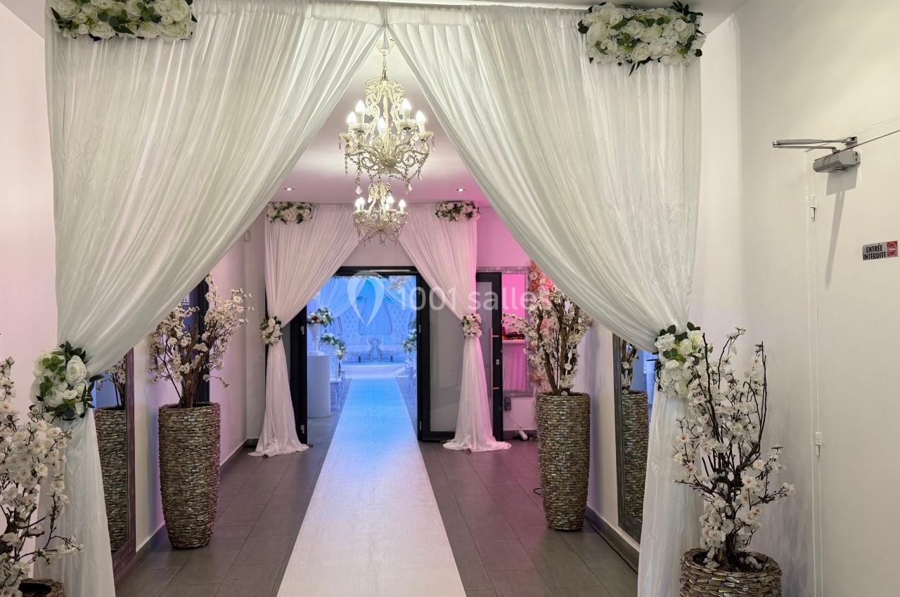 Allée décorée de rideaux blancs, lustres et arrangements floraux menant à une porte vitrée.