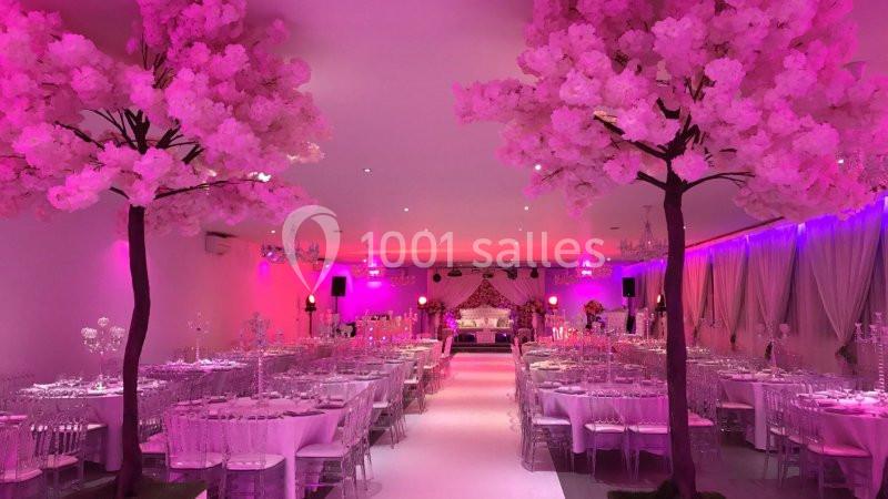 DECO ARBRE CERISIER Salle de réception décorée avec des tables dressées, éclairage rose et arbres artificiels fleuris.
