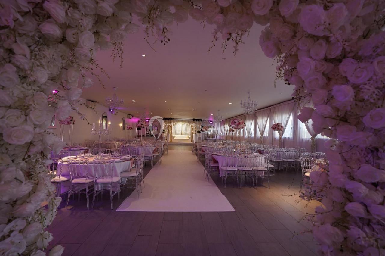 DECO ARCHE FLORALE Salle de réception décorée pour un mariage, avec des tables élégantes, des fleurs blanches et une arche florale au premier…