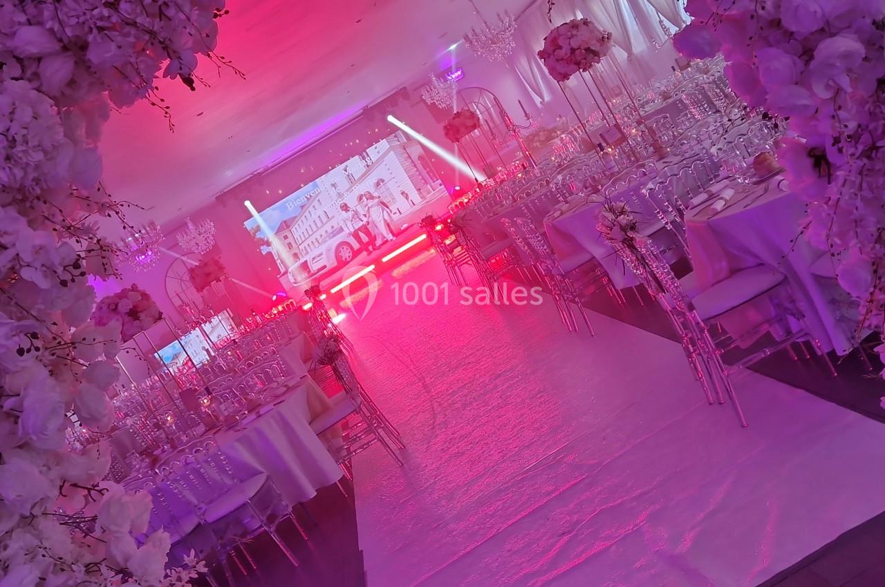 DECO ECRAN LED Salle de réception décorée avec des fleurs blanches, des tables dressées et un éclairage rose dominant.