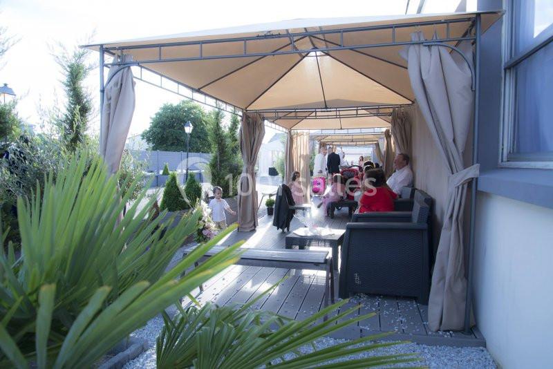 ESPACE EXTERIEUR Des personnes assises et debout sous des pergolas avec rideaux, dans un espace extérieur aménagé avec des plantes.