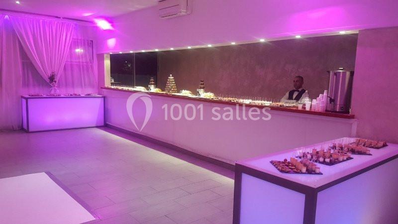 NOTRE BAR Salle de réception avec buffet éclairé par des lumières violettes, tables garnies de petites bouchées.