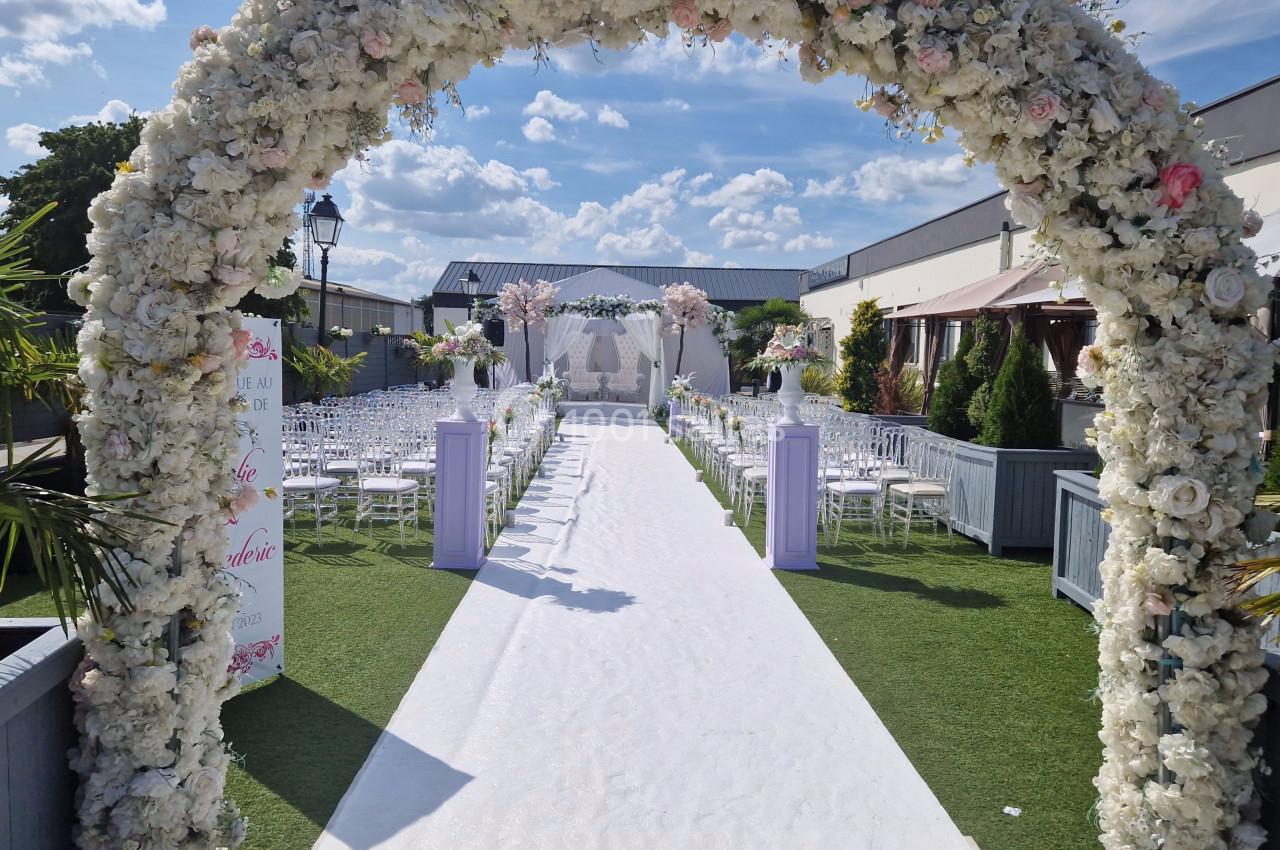 NOTRE BEL ESPACE EXTRERIEUR Allée centrale décorée de fleurs blanches et roses menant à une arche pour une cérémonie en extérieur par temps ensoleillé.