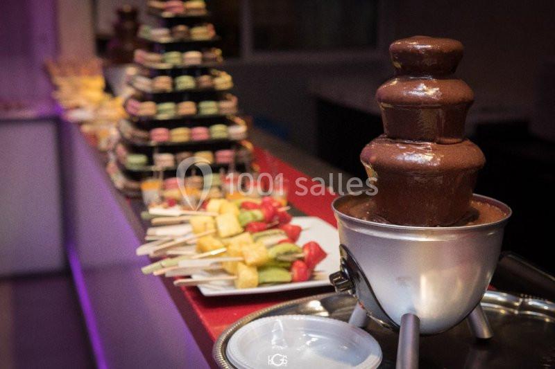 NOTRE FAMEUX BUFFET DESSERT Fontaine de chocolat avec des brochettes de fruits et des macarons disposés sur une table de buffet.