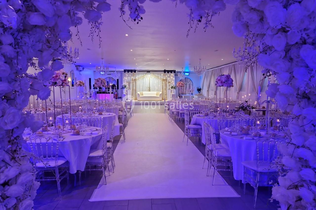 NOUVELLE DECORATION 2024 Salle de réception décorée avec des fleurs blanches, tables élégantes et éclairage bleu, centrée sur une estrade.