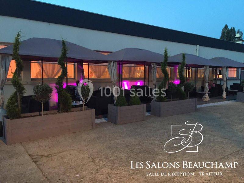 TERRASSE EXTERIEUR Terrasse aménagée avec des tentes, des plantes en bacs et un éclairage violet, devant un bâtiment moderne.