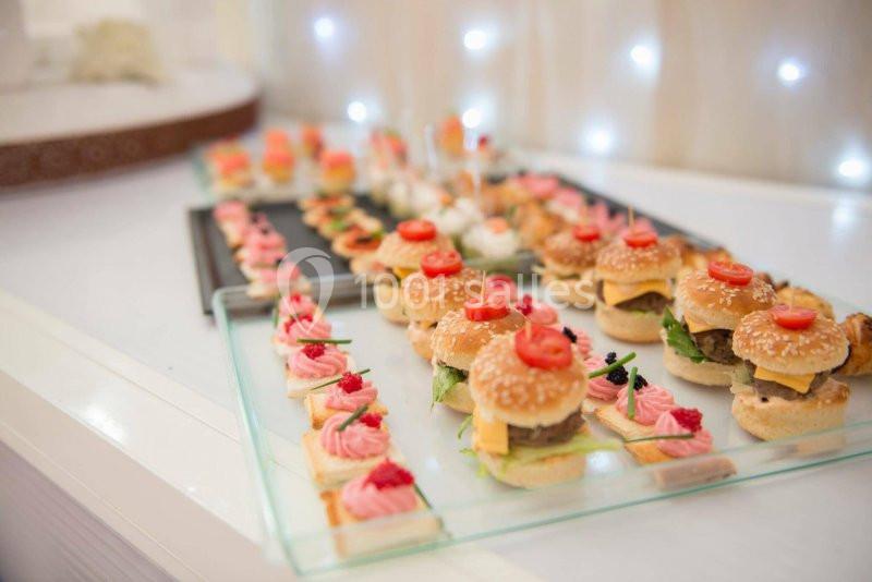 VIN D HONNEUR Plateau de mini-burgers et amuse-bouches variés disposés sur une table, éclairée par des lumières en arrière-plan.