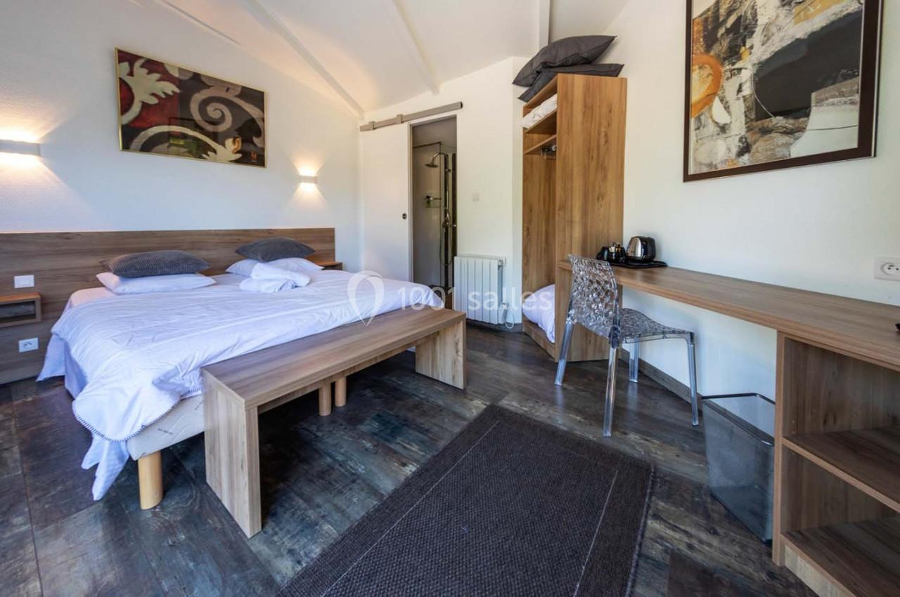 Location salle Saint-Aignan-de-Cramesnil (Calvados) - La Jalousie #21 Chambre lumineuse avec lit double, bureau en bois, chaise, armoire ouverte et décoration murale abstraite.