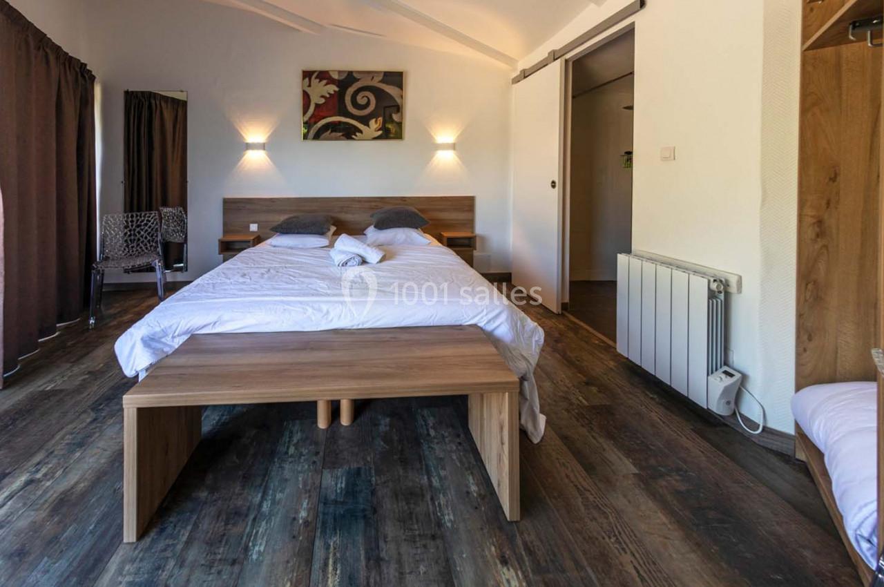 Location salle Saint-Aignan-de-Cramesnil (Calvados) - La Jalousie #22 Chambre lumineuse avec lit double, parquet en bois, éclairage mural et rideaux sombres.